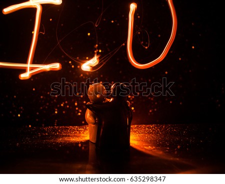 Two young lovers paint a heart on fire. Silhouette of couple and Love words on a dark background. Love concept