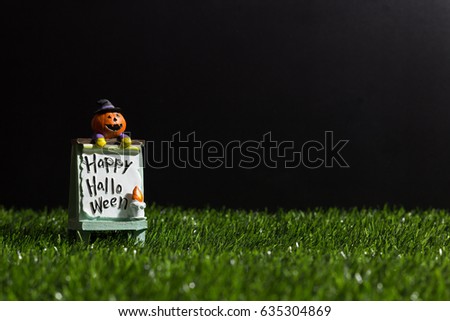 Pumpkin Ghost Doll on Stand Sidewalk Sign White Board with Message  "Happy Halloween" Paperweight on Artificial Grass at Dark Night. Copy Space for Text. Idea Concept for Halloween Background.