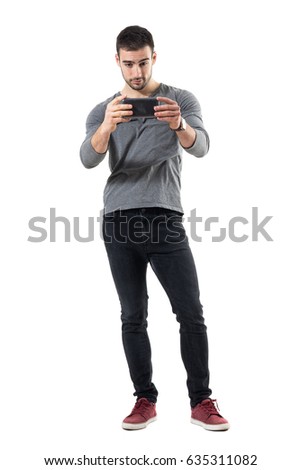 Young trendy casual man recording video with smart phone. Full body length portrait isolated on white studio background. 