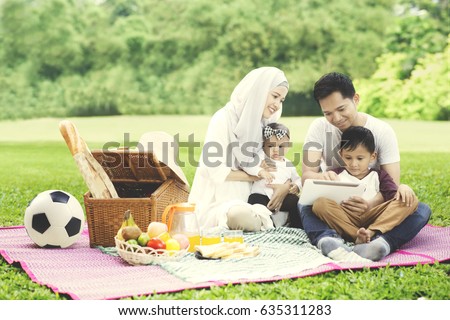 Picture of Muslim family using a digital tablet while picnicking in the park