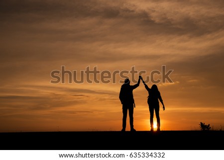 Silhouette of two couple (backpacker) holding hands,raise their hands to the sky,against sunset background.