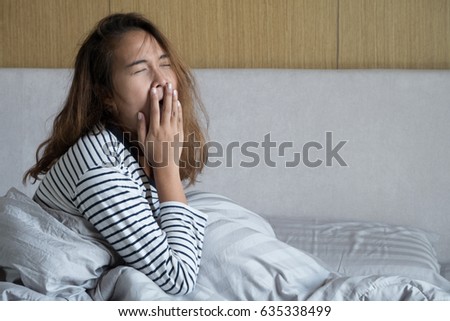 Beautiful young Asian woman with long curry hair yawn in the morning after wake up on bed. Portrait of woman in bedroom.