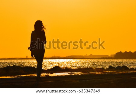 Young girl walking alone near seashore at sunset, silhouette.