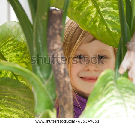 dieffenbachia, portrait, little girl seven years old, surrounded by leaves diffenbachia, botanical garden, looks camera, smiling, long wheat hair, happy child, bright day, lilac jacket, front, hide