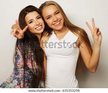 Two young girl friends standing together and having fun. Over white background.