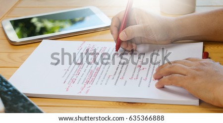 hand holding red pen over proofreading text on table Royalty-Free Stock Photo #635366888