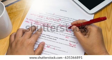 hand holding red pen over proofreading text on table Royalty-Free Stock Photo #635366891
