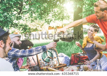 Group of friends having a picnic while eating and drinking wine in a park - Happy people having fun at backyard party on a sunny day - Friendship concept 