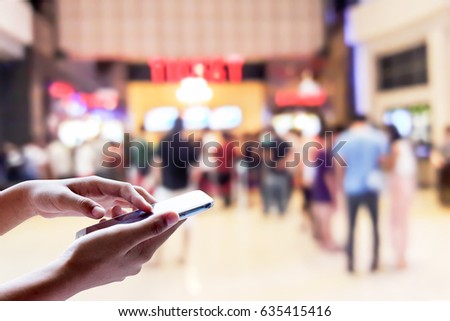 Man use mobile phone, blur of people in the movie ticket line as background.