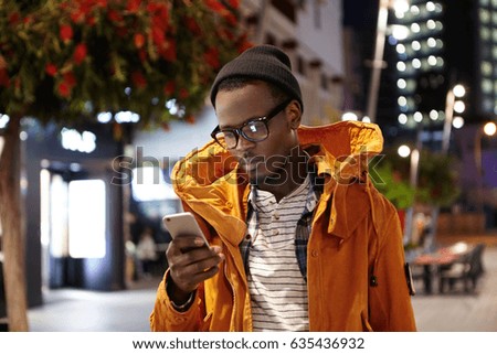 People, lifestyle, travel, tourism and modern technology. Tired young African American man using mobile phone for requesting cab via online taxi service app to get to hotel after long flight