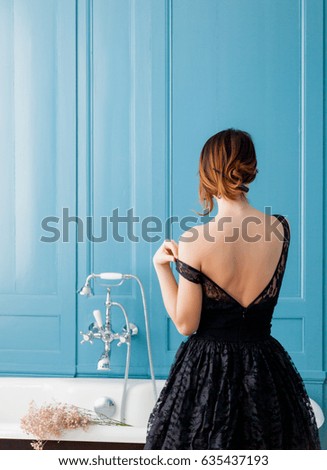 photo of beautiful young woman standing near bath and taking her dress off