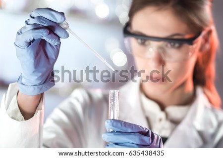 Life scientists researching in laboratory. Focused female life science professional pipetting solution into the glass cuvette. Lens focus on researcher's eyes. Healthcare and biotechnology concept. Royalty-Free Stock Photo #635438435