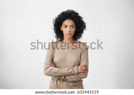 Indoor shot of angry grumpy young mixed race female dressed casually keeping arms folded, looking at camera with strict and skeptical expression, doesn't believe excuses of her unfaithful boyfriend Royalty-Free Stock Photo #635442119