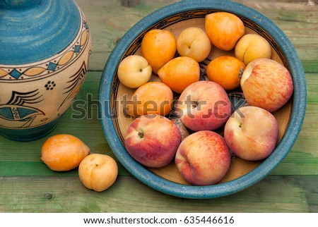 Still life vase and  fruits on ceramic dish on green shabby wooden  background.Retro style. Peaches, apricots and loquats. First fruits Symbols of Jewish holiday-Shavuot  in Israel.