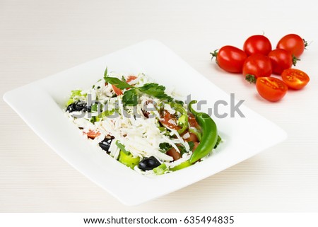 Traditional classic Shopska salad with tomatoes, peppers, cucumbers and cheese in white dish on white wooden table. Bulgarian cuisine, Balkan culture