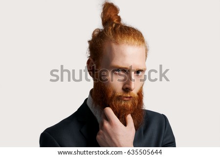 Effective and talented businessman with red hair look into the camera with strong sight and hold his beard by hand. Man think about debts and business development. Serious emotion concept. Top manager