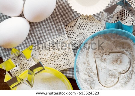 Baking ingredients on a lace cloth: eggs, flour in a bowl with a heart shape, cookie cutters. Top view flat lay