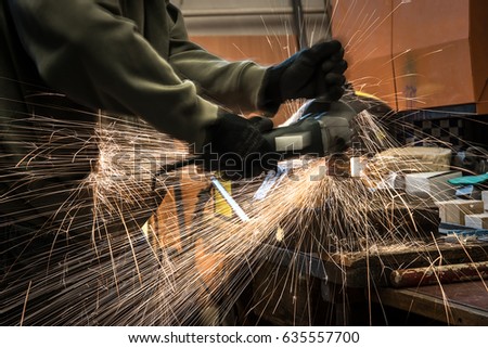 Man working with electric grinder tool on steel structure in workshop