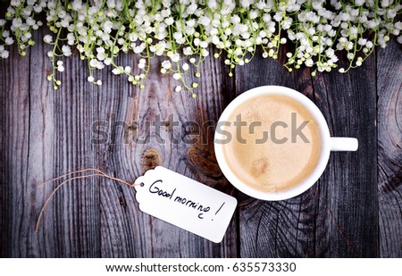 White cup with coffee on a gray wooden surface, top view, near a tag with an inscription good morning, decoration with flowers lilies of the valley