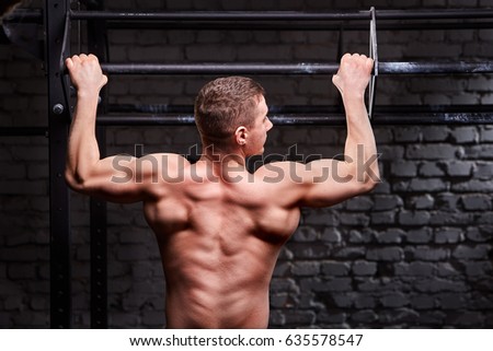 Rear view photo of the young muscular male doing exercises on horizontal bar against brick wall at the cross fit gym.