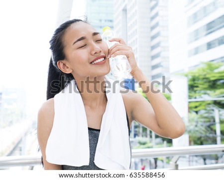 Asian woman in sport wear raised a water bottle to her face during outdoor workout on city street. Healthy woman taking a break after running workout.