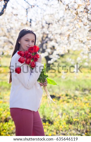 Portrait of a beautiful young girl in a spring garden with a red tulip flower in hands