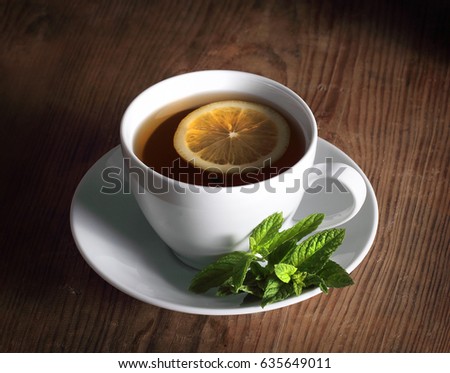 Tea drink in a white cup next to lies mint and spices
