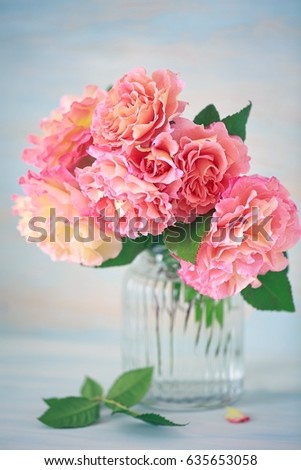 Delicate beautiful roses from a garden in a glass vase on a blue background.