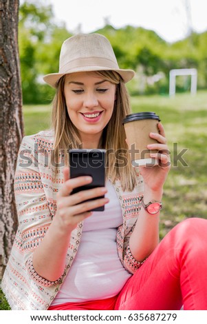 Portrait of a smiling beautiful woman texting with her phone in the garden.  smiling beautiful woman texting with her phone. Pretty brunette texting in the park on a sunny day