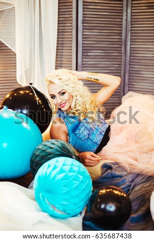 Beautiful young girl with long curly blond hair. A girl in an airy tutu with colorful multicolored balloons and pompoms