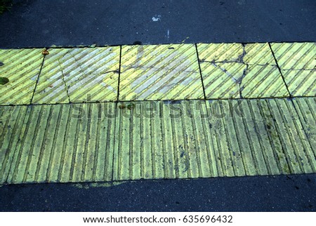 Cracked yellow tactile tiles on asphalt road. Damaged warning tiles on sidewalk