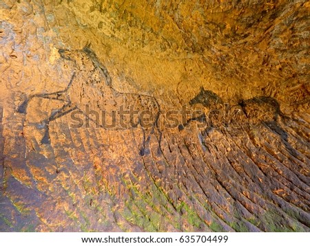 Discovery of prehistoric paint of horse in sandstone cave. Spotlight shines on historical human painting. Black carbon horses on sandstone wall. Paint of hunting,  prehistoric picture