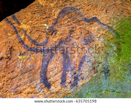 Prehistoric art of mammoth in sandstone cave. Spotlight shines on historical painting. Black carbon mammoth on sandstone wall. Paint of human hunting,  prehistoric picture. Discovery of human history