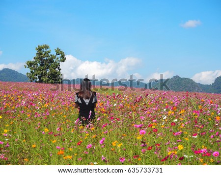 Back view of young woman standing and arms crossed near cosmos flowers in the garden