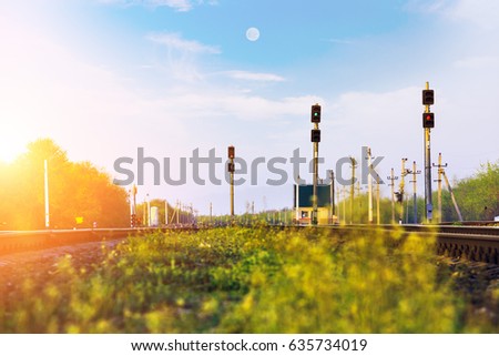 Railway station at sunset. Green grass and blue sky. Traffic lights shows green, red signal on railroad. Prohibiting signal. Regulation and control of movement. Travel by train. Rail transportation.
