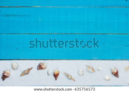 Collection of seashells in sand border on antique rustic teal blue wood background; blank wooden beach sign with copy space