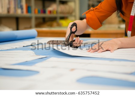 closeup photo of profession jobs female tailor cutting clothing samples through scissors and cardboard pattern drafts paper in the factory design office studio. Royalty-Free Stock Photo #635757452