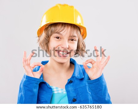 Emotional portrait of attractive girl wearing safety yellow hard hat. Beautiful child making ok gesture and looking at camera. Funny smiling child - engineer, construction worker or architect.