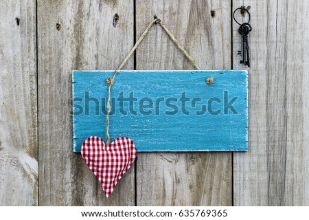 Blank antique rustic teal blue wood sign hanging by rope on wooden door with red and white checkered heart and keys; Valentines Day, love, home and family concept background with painted copy space