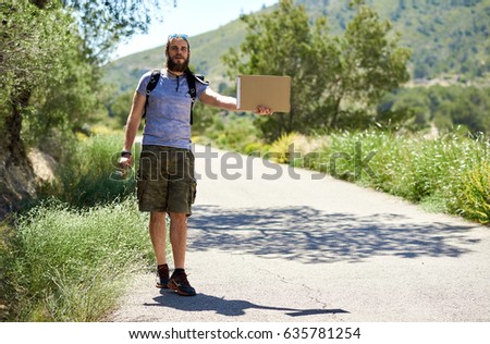 Hitch-hiking traveler with a blank cardboard sign on a mountain road. Budget travel. Auto stop
