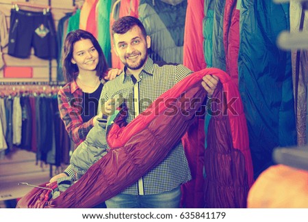 Smiling couple choosing new sleeping bag in sports equipment store

