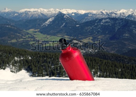 Drinking bottle of a hiker cooling down in snow at a warm day in spring; in the blurred background the mountains of the bavarian and tyrolean alps