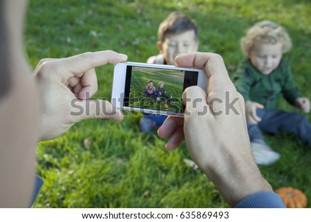 Men's hands holding a smartphone and making photo of happy children. Father taking pictures of his children on the phone in nature. Closeup