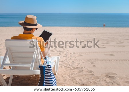 Back view of man sitting using touch screen tablet pc. Beach sunny seaside outdoors background. Travel modern lifestyle business connectivity, selfie photography, online shopping or playing game