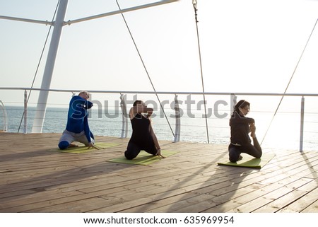 group of young people practicing in an outdoor yoga class. morning yoga exercices on wooden pier, sea background 