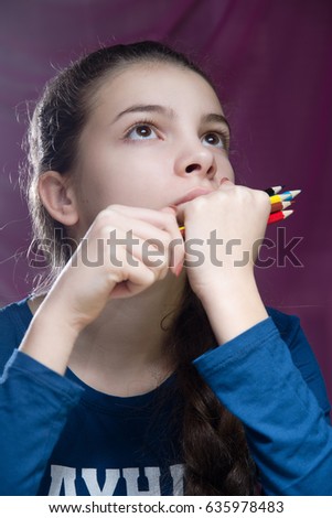 Portrait of charming girl that holds the pencils and looks up. Vertical colour photo. On a pink background