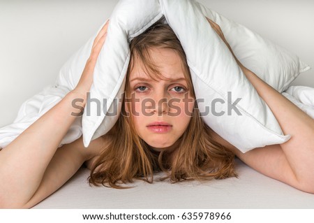 Young woman in bed covering ears with pillow because of noise Royalty-Free Stock Photo #635978966