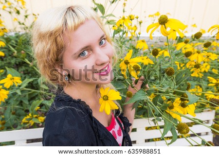 Closeup of young woman smiling by tall sunflower yellow daisy flowers on bench