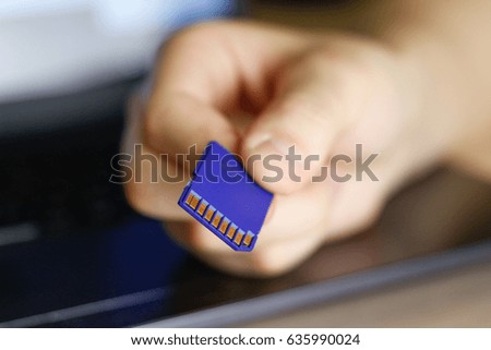 Hand holds SD memory card. Blue