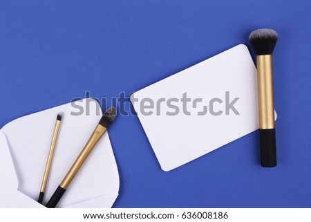 Beauty background. Make up brushes and white envelope with blank card. Top view. Flat lay.